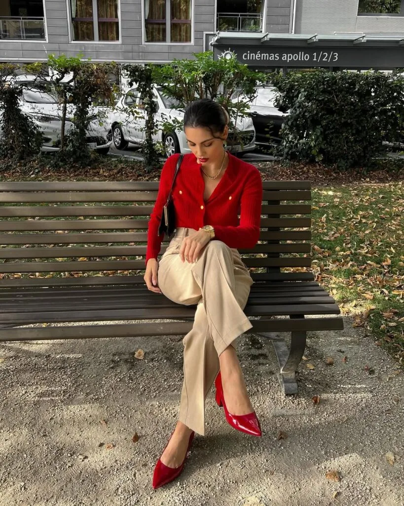 A fitted red cardigan with gold buttons styled with beige trousers, red heels, and a matching red handbag for a classic Valentine’s outfit.