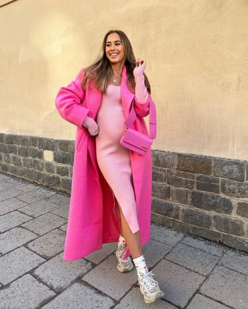 A pink ribbed midi dress styled with chunky sneakers, an oversized pink coat, and a matching shoulder bag for a sporty Valentine’s Day outfit.